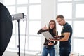 Photographer explaining about the shot to his assistant in the studio and looking on laptop. Teamwork and brainstorm