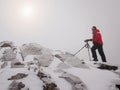 Photographer with eye at viewfinder of camera on tripod stay on snowy cliff and takes photos.