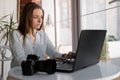 Photographer girl using laptop sitting at cafe, typing on keyboard, Professional photo camera lying on table. Female