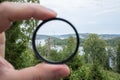 Photographer hand holds a polarizing filter, against the backdrop of trees, sky and sea. Royalty Free Stock Photo