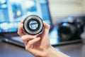 Photographer is holding a photography lens in his hand, camera and laptop in the blurry background Royalty Free Stock Photo
