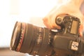 Photographer is holding a professional camera with telephoto lens in his hand, laptop in the blurry background Royalty Free Stock Photo