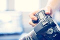 Photographer is holding a professional camera with telephoto lens in his hand, laptop in the blurry background Royalty Free Stock Photo