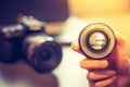 Photographer is holding a photography lens in his hand, camera and laptop in the blurry background