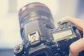 Photographer holds a reflex camera with telephoto lens in his hand. Table and laptop in the blurry background Royalty Free Stock Photo