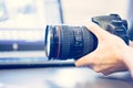 Photographer holds a reflex camera with telephoto lens in his hand. Table and laptop in the blurry background Royalty Free Stock Photo