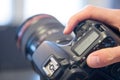 Photographer holds a reflex camera with telephoto lens in his hand. Table and laptop in the blurry background Royalty Free Stock Photo