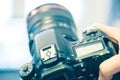 Photographer holds a reflex camera with telephoto lens in his hand. Table and laptop in the blurry background Royalty Free Stock Photo