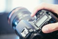 Photographer holds a reflex camera with telephoto lens in his hand. Table and laptop in the blurry background Royalty Free Stock Photo