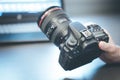 Photographer holds a reflex camera with telephoto lens in his hand. Table and laptop in the blurry background Royalty Free Stock Photo