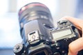 Photographer holds a reflex camera with telephoto lens in his hand. Table and laptop in the blurry background Royalty Free Stock Photo