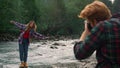 Photographer photographing woman at river. Girl making funny grimace at camera