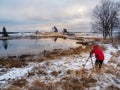 The photographer shoots a wonderful snowy winter landscape with authentic house on the shore in the Russian village