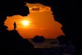 Photographer standing in the cave near the beach at red sky sunset Royalty Free Stock Photo