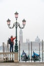 Photographer stands at the lamppost with gondolas moored by Saint Mark square and with San Giorgio di Maggiore church