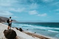 Photographer with stative and camera staying on the rock and enjoying coastal landscape of sand dunes, volcanic cliffs Royalty Free Stock Photo