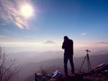 Photographer stay with camera ind hands at tripod on rock Royalty Free Stock Photo