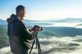 Photographer takes photos with camera on tripod on rocky mountain peak. Beautiful misty sunrise and valley view over Royalty Free Stock Photo