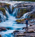 Photographer takes picture of Bruarfoss Waterfall, secluded spot with cascading blue waters. Colorful sunset in Iceland, Europe.