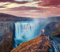 Photographer takes picture on the cliff on falling water of most powerful waterfall in Europe - Dettifoss.