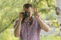 Photographer takes pictures against the background of greenery. Front view. Victory hand