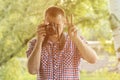 Photographer takes pictures against the background of greenery. Front view. Victory hand