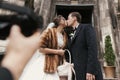 Photographer taking photo of gorgeous bride in coat and stylish groom near church door after wedding ceremony.  happy newlywed Royalty Free Stock Photo