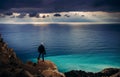 Photographer traveler stands on the edge of a cliff above the turquoise sea at sunset