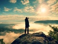 Photographer with tripod on cliff shadowing eyes and thinking. Heavy fogy landscape,