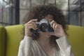 Curly haired photographer woman holding her camera in a cafe and shooting Royalty Free Stock Photo