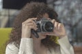 Curly haired photographer woman holding her camera in a cafe and shooting Royalty Free Stock Photo