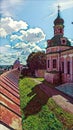 Photographic art picture of orthodox monastery and rusty roof of its surrounding wall under blue cloudy sky in summer
