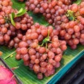 a photography of a bunch of grapes on a banana leaf, grocery store display of red grapes and other fruits on banana leaves Royalty Free Stock Photo