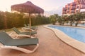 Photography of deck chair and umbrella and a pool, a residential area during the sunset with palms and pool