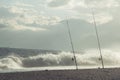 Fishing in the sea from the coast - two fishing rods attached to the sand of the beach - dramatic waves hitting the coastline Royalty Free Stock Photo