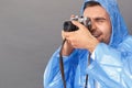 Photography Hobby. Young man in raincoat studio standing on grey with film camera taking photos excited close