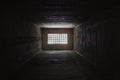 Light behind barred window in the dark prison cell - empty jail interior with grey concrete walls Royalty Free Stock Photo