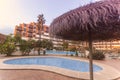 Photography of un umbrella and a pool, a residential area during the sunset with palms and pool