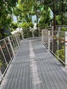 a photography of a walkway with a fence and a bench, balustraded walkway with metal grate and railings leading to trees Royalty Free Stock Photo