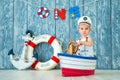 Photoshoot for a boy of one year. Little sea captain, sailor on toy ship with steering wheel. Sea anchor and lifebuoy on gray Royalty Free Stock Photo