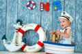 Photoshoot for a boy of one year. Little sea captain, sailor on toy ship with steering wheel. Sea anchor and lifebuoy on gray