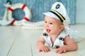 Photoshoot for a boy of one year. Little sea captain, sailor on toy ship with steering wheel. Sea anchor and lifebuoy on gray Royalty Free Stock Photo