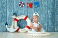 Photoshoot for a boy of one year. Little sea captain, sailor on toy ship with steering wheel. Sea anchor and lifebuoy on gray