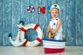 Photoshoot for a boy of one year. Little sea captain, sailor on toy ship with steering wheel. Sea anchor and lifebuoy on gray