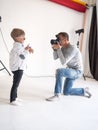 Photographer man photographs a little boy in a white shirt on a white background. Royalty Free Stock Photo