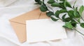 Photostock wedding styled composition. Feminine envelope mockup scene with ruscus leaves, silk ribbon, blank greeting card, on cre