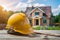 PhotoStock Yellow safety helmet on table with backdrop of house under construction photo Royalty Free Stock Photo