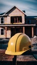 PhotoStock Yellow safety helmet on table with backdrop of house under construction photo Royalty Free Stock Photo