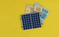 Photovoltaic panel , money and plug wire isolated on yellow background. olar panel with varied values of Brazilian money Royalty Free Stock Photo