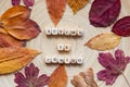 The phrase AUTUMN IS COMING made of wooden cubes on a wooden background with colorful autumn leaves. Royalty Free Stock Photo